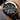 Black wristwatch with silver accents on a person's wrist against a dark background