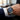 Close-up of a wrist wearing a silver watch with a blue face, set against a blurred indoor background.