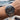 Silver watch with black dial on a wrist, blurred background of water and boats