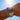 Gold wristwatch with a blue dial on a person's wrist against a clear blue sky.