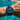 Blue wristwatch with a detailed face on a wrist above clear blue water.