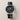 Luxury watch with black leather strap and detailed face on a light beige background