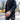 Person wearing a dark denim jacket and watch on a city street with taxis in the background