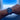 Person wearing a blue wristwatch with a window view of clouds and blue sky.